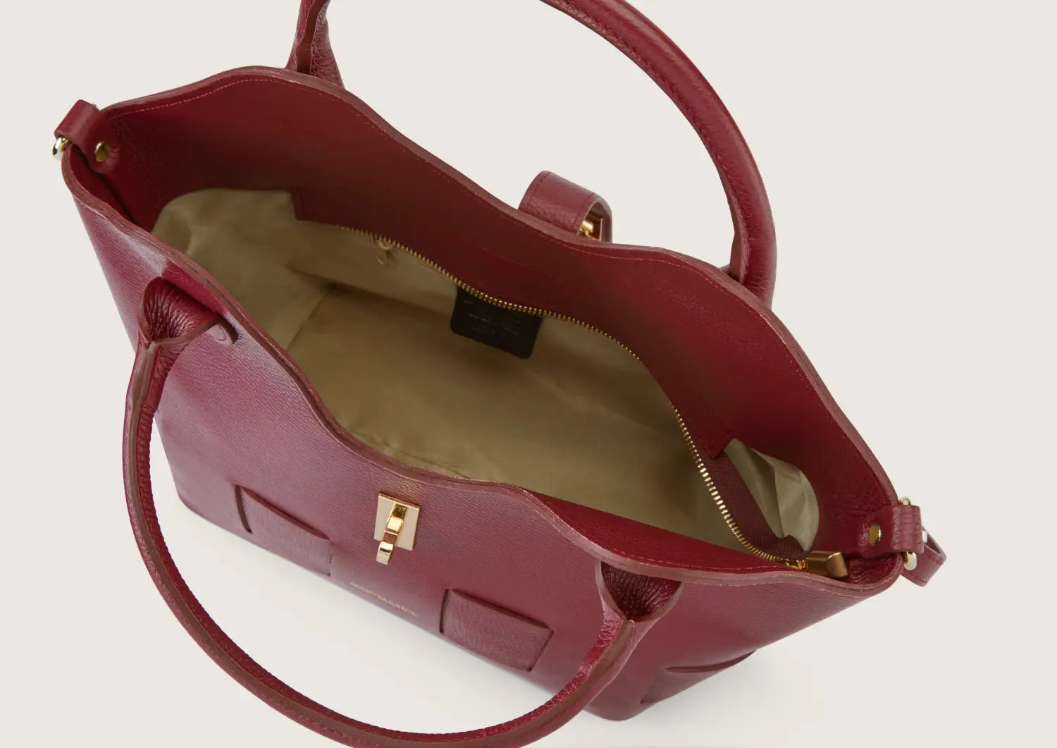 Close-up of the dark red leather handbag showcasing the durable top zip closure with metallic detailing.
